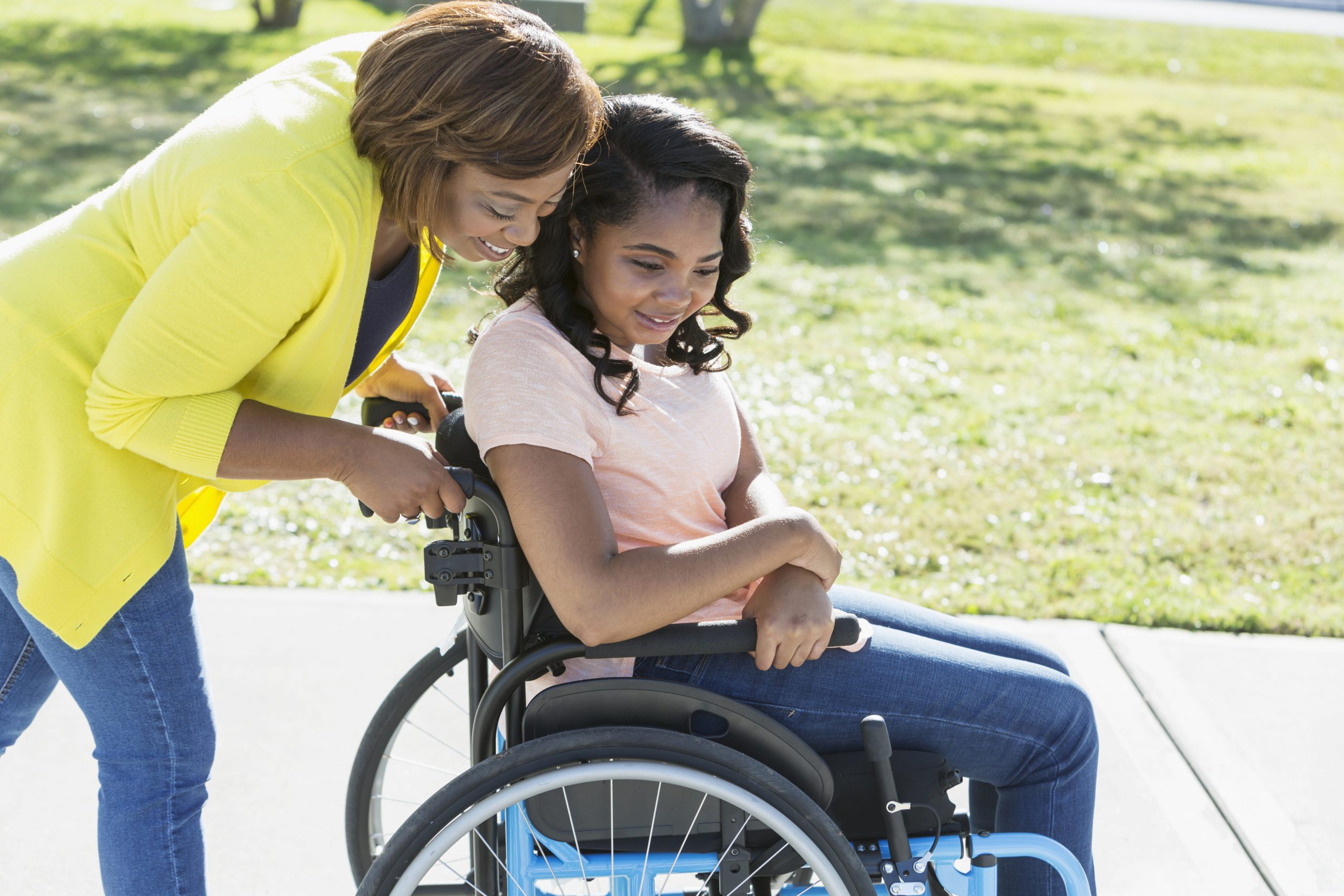 An African-American woman walking with her daughter who is a paraplegic in a wheelchair, outdoors. She is 15 years old, mixed race African-American and Hispanic.